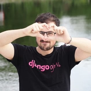 Thibaud Colas making a heart shape with his fingers in front of his face while wearing a Django Girls t-shirt.